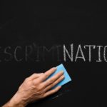 Male hand cleaning word DISCRIMINATION on chalkboard, leave word NATION